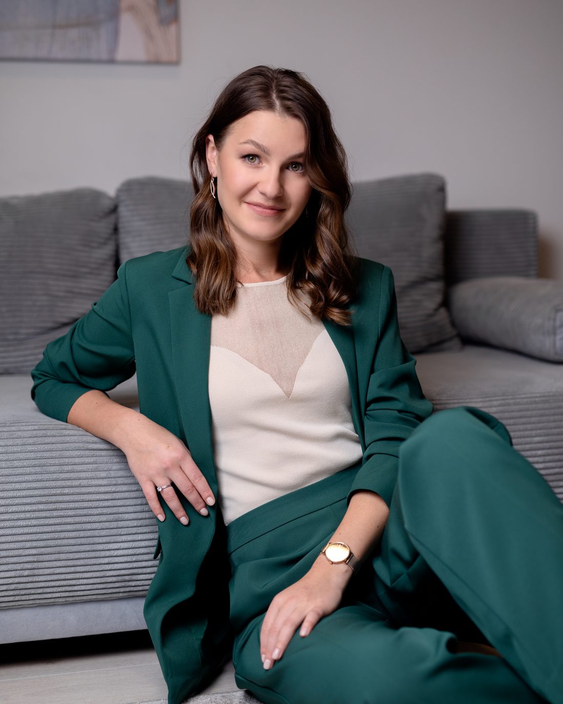 Natalia in a green suit, smiling, sitting on the floor against a grey sofa